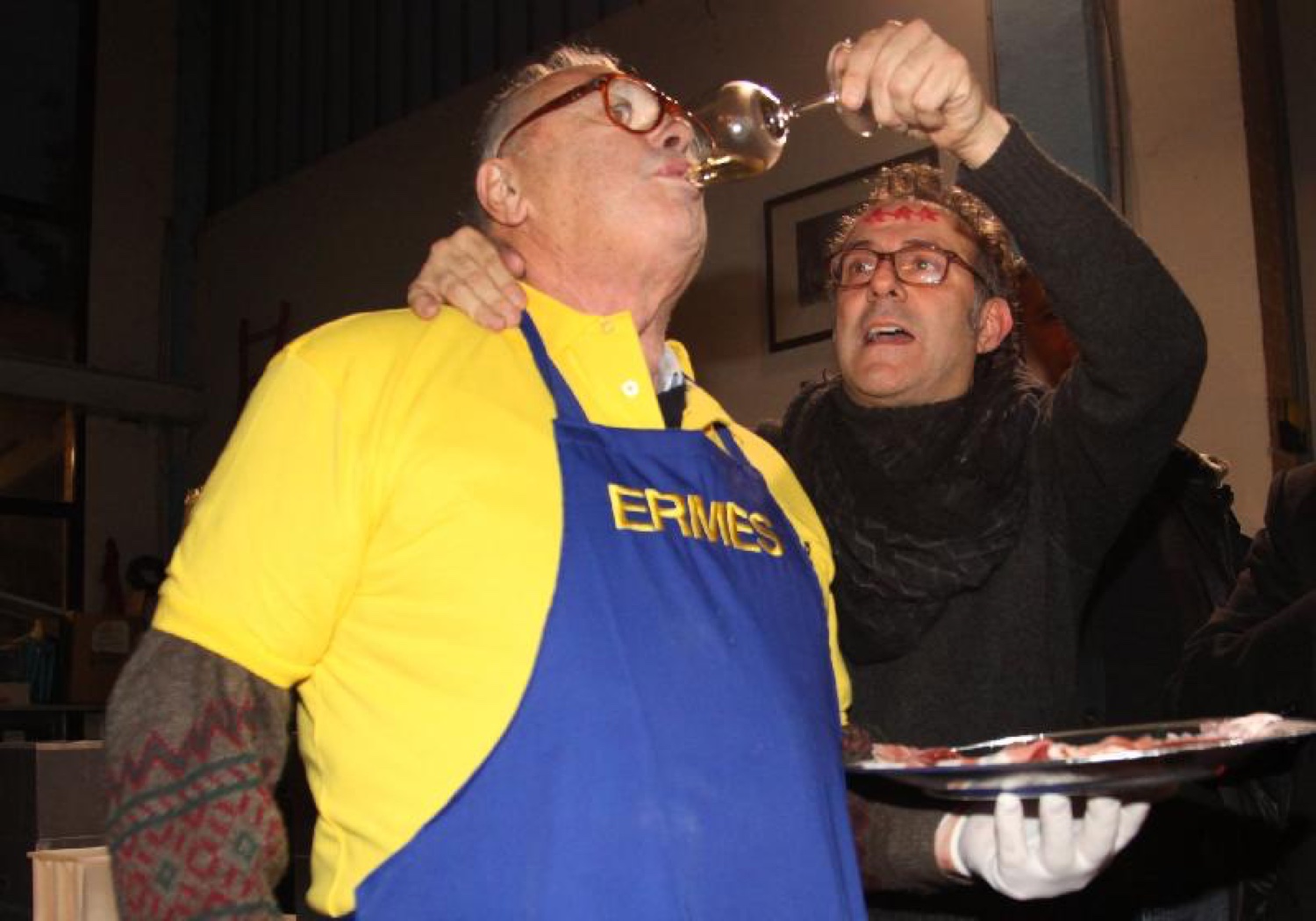 Ermes, nel suo grembiule giallo, beve un sorso di vino mentre Massimo Bottura gli porge il calice